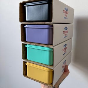 May include: A stack of four colorful plastic toolboxes in their cardboard packaging. The boxes are black, purple, teal, and yellow. The boxes are labeled "TOOLBOX T-80".