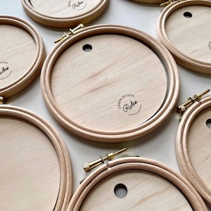 May include: Five wooden embroidery hoops with a gold screw closure. The hoops are all the same size and have the words "Cross Stitch Rules" printed on them.