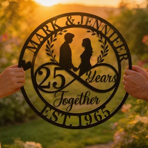 May include: Black metal wall art with the names "Mark & Jennifer" and the text "25 Years Together EST. 1965". The design features silhouettes of a couple holding hands, with a floral wreath and an infinity symbol.