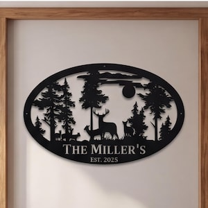 May include: An oval black metal wall sign featuring a laser-cut forest scene with silhouettes of deer, pine trees, and a moon. The text "THE MILLER'S" is centered below the scene, followed by the text "EST. 2025" in a clean, sans-serif font.