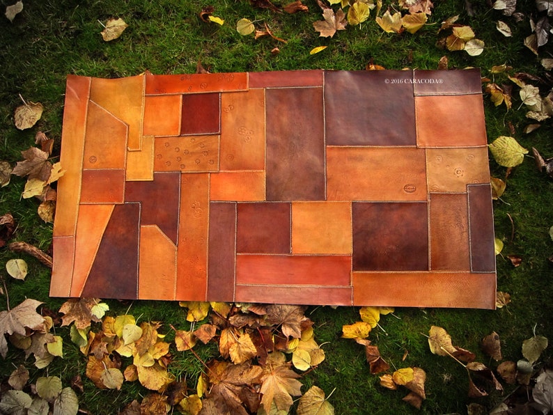 Peut inclure: Un article rectangulaire en patchwork de cuir dans les tons marron, orange et beige. Le motif est compos&eacute; de diverses formes g&eacute;om&eacute;triques cousues ensemble. Le texte "&copy; 2016 CARACODDA" est visible dans le coin sup&eacute;rieur droit. L'article est pr&eacute;sent&eacute; sur un lit d'herbe verte et de feuilles mortes.