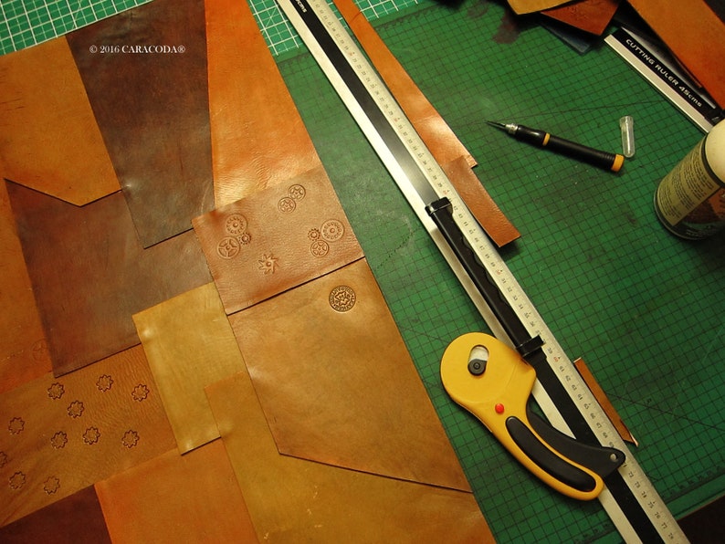 Peut inclure: Un espace de travail artisanal avec diverses pi&egrave;ces de cuir marron de diff&eacute;rentes formes et nuances. Un cutter rotatif jaune, une r&egrave;gle m&eacute;tallique et un cutter sont sur un tapis de coupe vert. Certaines pi&egrave;ces de cuir ont des motifs estamp&eacute;s.