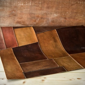 Peut inclure: Un tapis en cuir patchwork dans les tons marron, beige et brun rouge&acirc;tre. Les pi&egrave;ces rectangulaires sont cousues ensemble avec du fil blanc. Le tapis est partiellement enroul&eacute;, r&eacute;v&eacute;lant sa texture et son design. Le fond est une surface en bois.