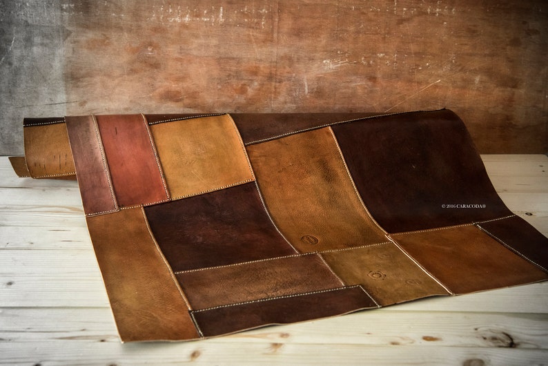Peut inclure: Un tapis en cuir patchwork dans les tons marron, beige et brun rouge&acirc;tre. Les pi&egrave;ces rectangulaires sont cousues ensemble avec du fil blanc. Le tapis est partiellement enroul&eacute;, r&eacute;v&eacute;lant sa texture et son design. Le fond est une surface en bois.