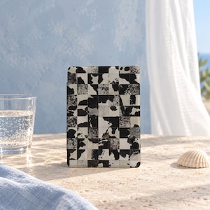 May include: A rectangular e-reader case featuring a black and white cow print pattern arranged in a grid of square tiles. The surface displays a mix of solid black, solid white, and mottled black and white patches across the entire front cover.
