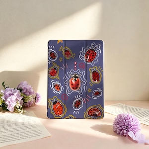 Pode incluir: Uma capa retangular para tablet com fundo roxo escuro apresentando um padrão repetitivo de joaninhas vermelhas com pintas pretas. As joaninhas são cercadas por contornos brancos desenhados à mão, estrelas amarelas e pequenos detalhes em espiral.