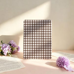 May include: A rectangular tablet case featuring a brown and white gingham check pattern. The case has a smooth, flat surface with vertical fold lines visible across the front, designed to protect a portable electronic device.