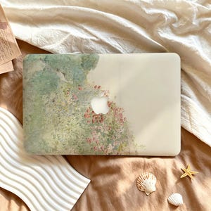 May include: A rectangular laptop case featuring a soft, impressionistic floral print with shades of sage green, pale pink, and cream. The design covers the left side of the case, leaving the right side a solid, translucent off-white finish.