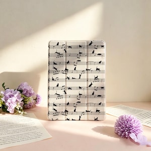 May include: A rectangular tablet case with a white background featuring a repeating black pattern of musical staff lines and various silhouettes of cats in different poses, including sitting, walking, and jumping across the musical notes.