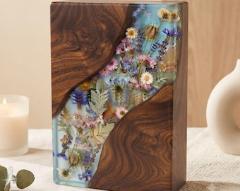 Peut inclure: Un bloc rectangulaire composé de bois brun foncé et de résine bleu clair translucide. La section en résine présente un arrangement intégré de diverses fleurs sauvages séchées, dont de la lavande, des marguerites et du feuillage.