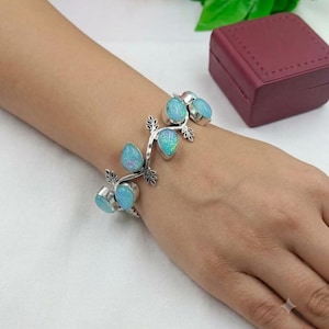 May include: A silver bracelet featuring a vine-like design with multiple teardrop-shaped iridescent blue stones. The metal links are shaped like small leaves, connecting the polished blue cabochons in a continuous, flexible arrangement.