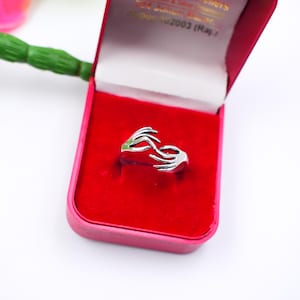 May include: A silver ring in a red jewellery box. The ring features a design of two hands embracing. The jewellery box is pink with the text "Khandaka Om Shree Jewellers" in gold lettering.