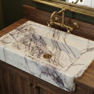 May include: A rectangular marble sink with purple veining sits atop a dark wood vanity. A gold faucet and a black soap dispenser are visible. The sink is a focal point in a bathroom setting.