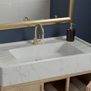 May include: A modern bathroom vanity with a white marble countertop and a rectangular sink. The faucet and mirror frame are gold-toned. A white towel hangs on a gold towel rack. The vanity is set against a dark blue wall.