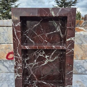 May include: A rectangular, burgundy marble shelf with two recessed compartments. The marble features white and light green veining throughout. The shelf is designed for storage or display, adding a touch of elegance to any space.