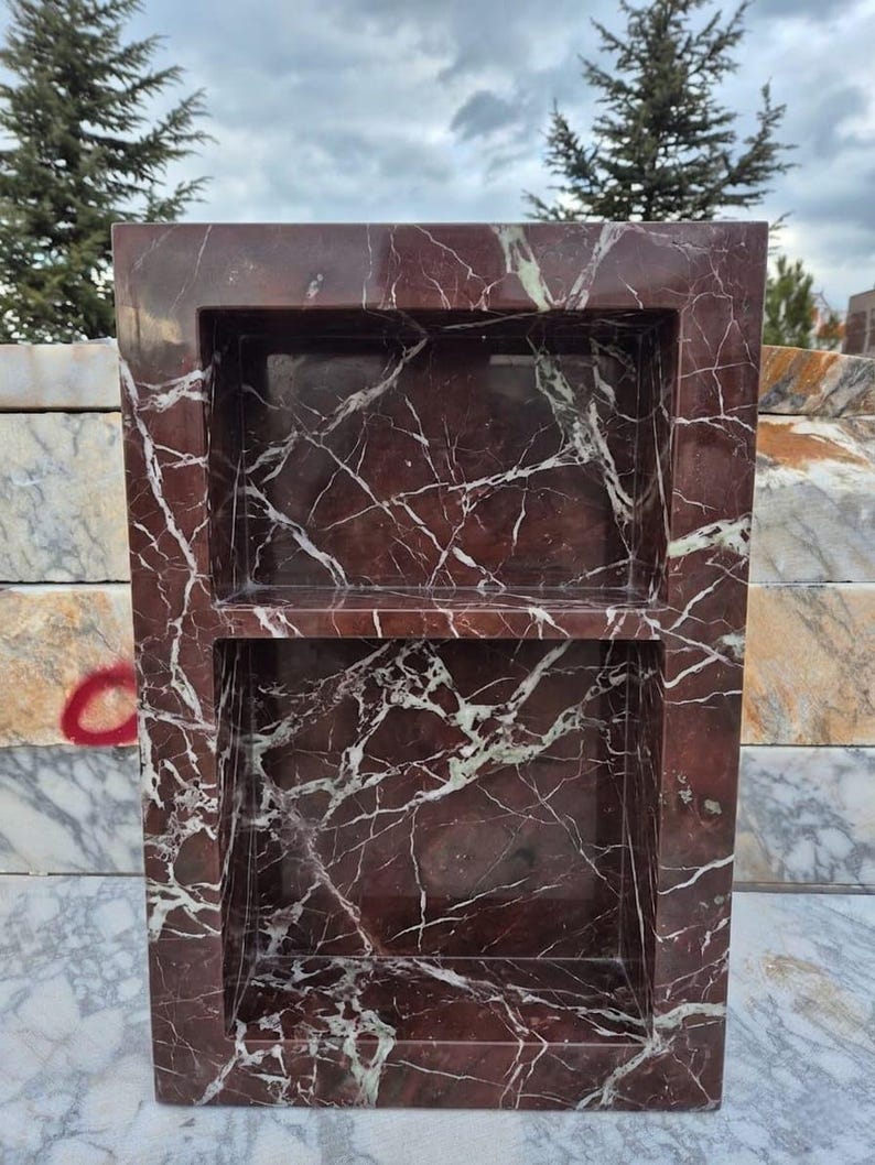 May include: A rectangular, burgundy marble shelf with two recessed compartments. The marble features white and light green veining throughout. The shelf is designed for storage or display, adding a touch of elegance to any space.