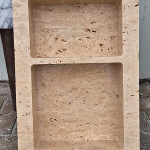May include: A rectangular, beige stone tray with two recessed compartments. The stone has a porous texture and a natural, earthy appearance. The tray is likely for decorative or functional use, such as holding soap or small items.