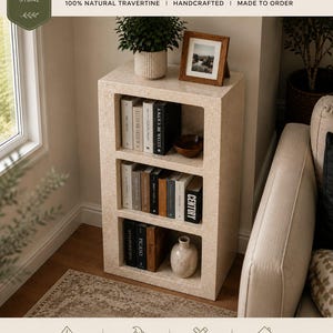 Pu&ograve; includere: Uno scaffale rettangolare in pietra di travertino con tre scomparti aperti. L'unit&agrave; in pietra beige porosa contiene vari libri, una piccola ciotola in legno e un vaso in ceramica. Il testo in alto recita TRAVERTINE STONE SHELF 100% NATURAL TRAVERTINE.
