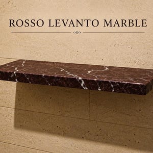 Könnte beinhalten: Ein rechteckiges Wandregal aus dunkelrotem Rosso Levanto Marmor mit ausgeprägter weißer Äderung. Das Regal ist an einer hellbeigen Steinwand montiert. Der Text ROSSO LEVANTO MARBLE ist in Schwarz über dem Regal aufgedruckt.