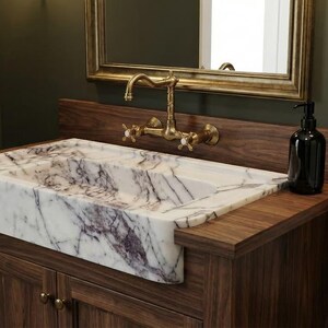 May include: A bathroom vanity with a marble sink, wooden cabinet, and gold fixtures. The sink has a white and purple pattern. A black soap dispenser and a white towel on a gold ring complete the scene.