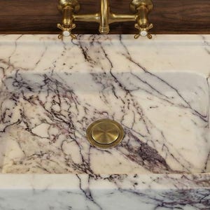 May include: A rectangular marble sink with a white and purple veined pattern. The sink has a brass drain cover and faucet. It is set on a wooden countertop with a brown glass bottle.