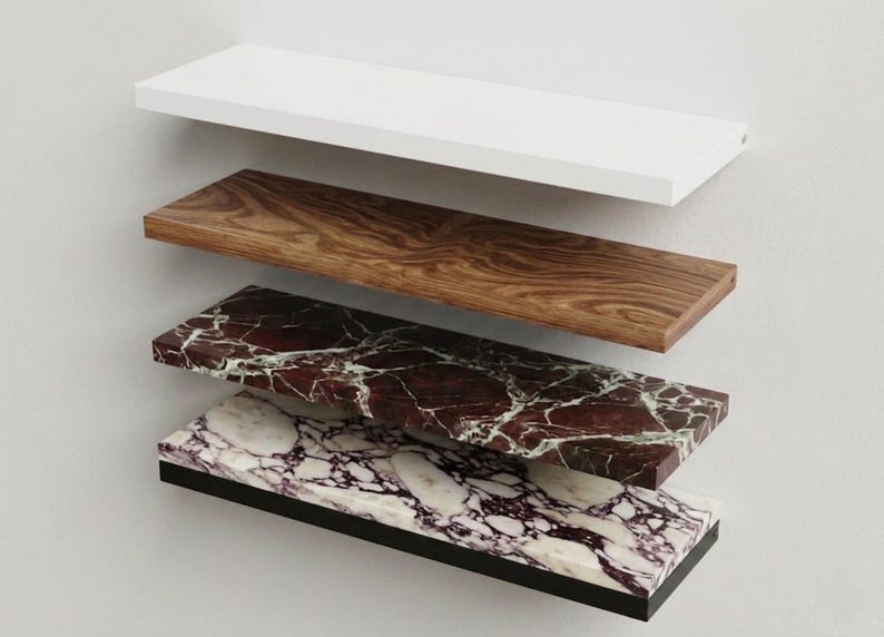 Pu&ograve; includere: Una pila di cinque mensole rettangolari sospese con finiture distinte: una mensola bianca solida, una con venature del legno, una in marmo rosso scuro con venature bianche, una in marmo bianco con venature viola e una mensola nera solida.