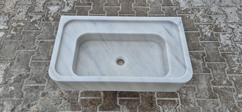 May include: A rectangular white marble sink with a rounded interior basin and a central drain hole. The sink has a smooth, polished surface and is designed for bathroom use.