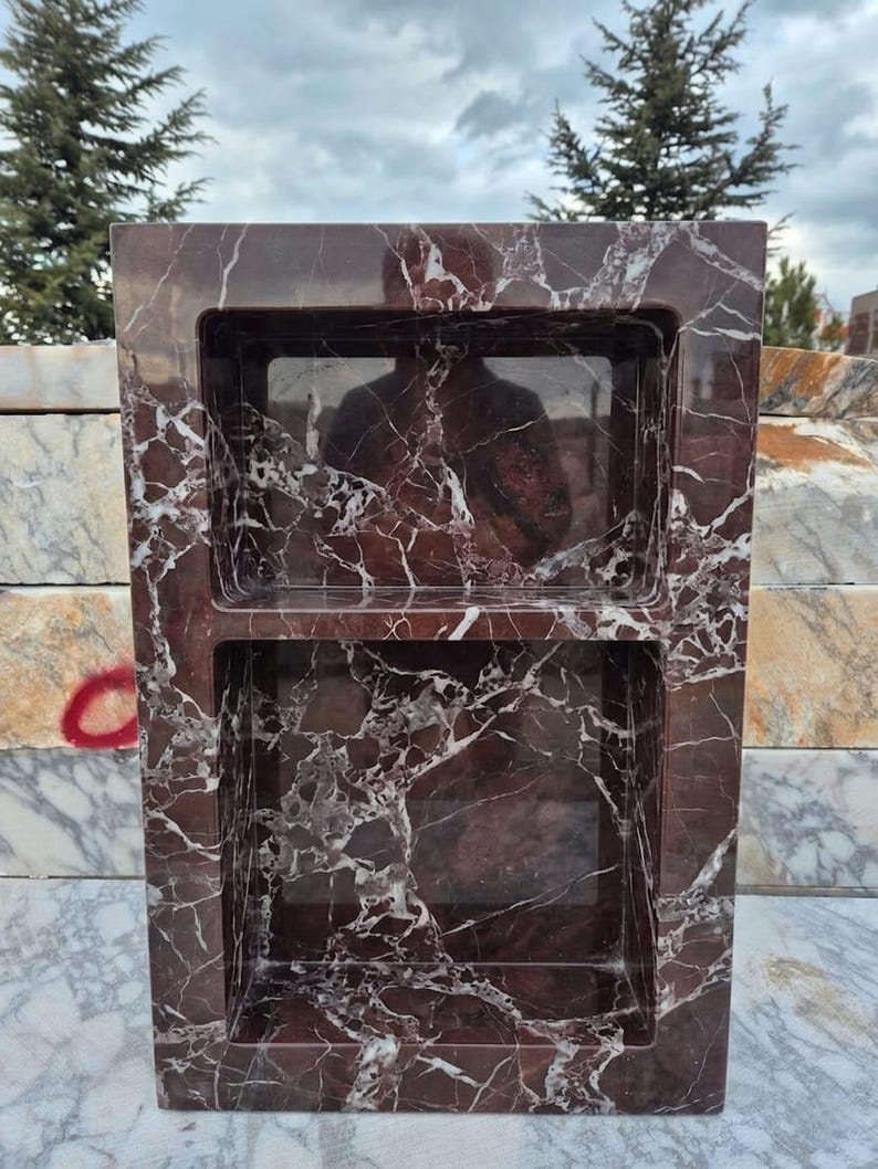 May include: A rectangular, dark red marble shower niche with two recessed shelves. The marble has a prominent white veining pattern. The niche is designed to be built into a shower wall for storage of toiletries.