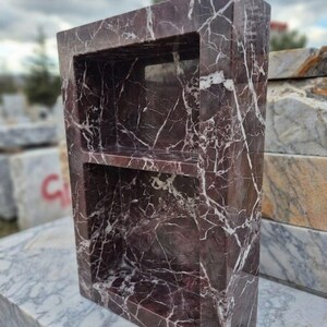 May include: A rectangular, freestanding marble shelf unit with two shelves. The marble is a deep burgundy color with white veining. The unit is designed to be recessed into a wall or used as a decorative storage piece.