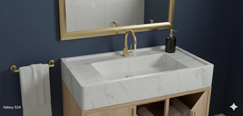 May include: A modern bathroom vanity with a white marble countertop and a rectangular sink. The faucet and mirror frame are gold-toned. A white towel hangs on a gold towel rack. The vanity is set against a dark blue wall.