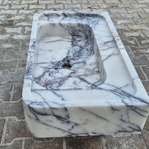 May include: A rectangular marble sink with a white base and dark gray veining. The sink has a rectangular basin with a drain hole. The sink is made of stone and is suitable for a bathroom.