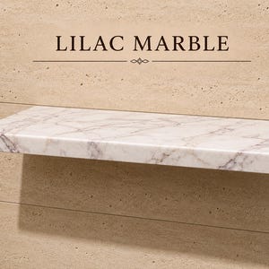 Pu&ograve; includere: Una mensola rettangolare sospesa in marmo bianco con venature lilla e grigie. La mensola &egrave; montata su una parete in pietra beige testurizzata. Il testo LILAC MARBLE &egrave; stampato in lettere marrone scuro sopra la mensola con una linea.
