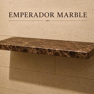 Pu&ograve; includere: Una mensola rettangolare sospesa in marmo Emperador marrone scuro con finitura lucida. La mensola &egrave; montata orizzontalmente su una parete in pietra beige chiaro. Il testo EMPERADOR MARBLE &egrave; stampato in nero sopra la mensola.