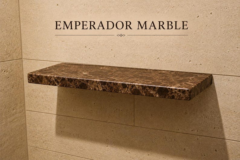 Pu&ograve; includere: Una mensola rettangolare sospesa in marmo Emperador marrone scuro con finitura lucida. La mensola &egrave; montata orizzontalmente su una parete in pietra beige chiaro. Il testo EMPERADOR MARBLE &egrave; stampato in nero sopra la mensola.