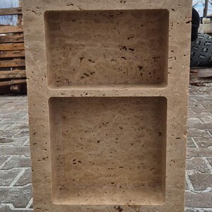 May include: A rectangular, beige stone shelf with two recessed compartments. The stone has a textured, porous surface. The shelf is freestanding and appears to be made of natural stone. The shelf is designed for storage or display.