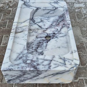 May include: A rectangular marble sink with a white base and intricate gray and purple veining. The sink has a rectangular basin and a smaller, recessed area. The sink is made of natural stone and is suitable for a bathroom.