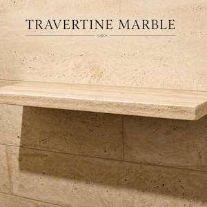 May include: A rectangular floating shelf made of beige travertine marble with a porous, natural stone texture. The shelf is mounted against a matching tiled wall. The text TRAVERTINE MARBLE is printed in black above the shelf.