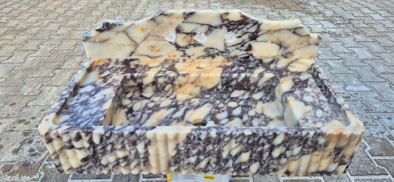 Pu&ograve; includere: Un lavabo rettangolare in marmo con un motivo color crema, marrone e viola. Il lavabo ha un bordo smerlato e tre fori per i rubinetti. Il lavabo &egrave; in pietra ed &egrave; adatto per un bagno.