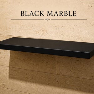 Pu&ograve; includere: Una mensola rettangolare sospesa in marmo nero montata su una parete piastrellata color beige. Il testo "BLACK MARBLE" &egrave; stampato in nero sopra la mensola, accompagnato da una linea orizzontale decorativa con un piccolo emblema centrato.