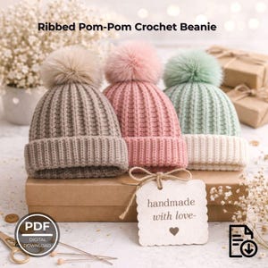 May include: Three ribbed pom-pom crochet beanies in neutral, pink, and mint green with matching faux fur pom-poms. A tag reads "handmade with love-". The text "Ribbed Pom-Pom Crochet Beanie" is at the top. A PDF digital download icon is in the lower left.