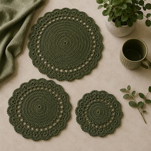 May include: Three olive green crochet placemats and coasters in varying sizes. The placemats and coasters have a circular design with a scalloped edge. A green mug and a small potted plant are also in the image.