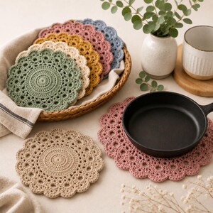 May include: A collection of round, crocheted coasters in various colors including sage green, mustard yellow, dusty rose, beige, and slate blue. The coasters feature a detailed, circular lace-like pattern with scalloped edges, arranged in a woven basket.