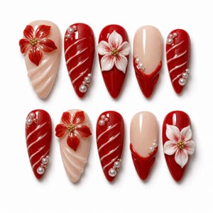 Puede incluir: Un juego de diez uñas postizas en forma de almendra con acabado brillante en tonos rojo intenso y nude. Los diseños incluyen flores tridimensionales rojas y blancas, líneas blancas diagonales en relieve y pequeños adornos de perlas blancas.