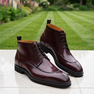 May include: A pair of dark burgundy leather ankle boots featuring a polished finish, a lace-up front with matching dark laces, a stitched apron toe design, a pull tab at the heel, and a solid black rubber sole with a low block heel.