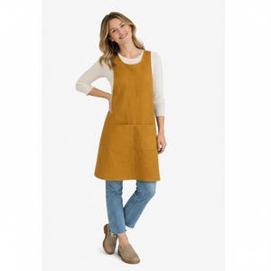 K&ouml;nnte beinhalten: Senffarbene Sch&uuml;rze mit zwei gro&szlig;en Vordertaschen. Die Sch&uuml;rze ist &auml;rmellos und hat einen runden Ausschnitt. Das Model tr&auml;gt ein cremefarbenes Langarmshirt und blaue Jeans. Die Sch&uuml;rze ist aus einem strukturierten Stoff.