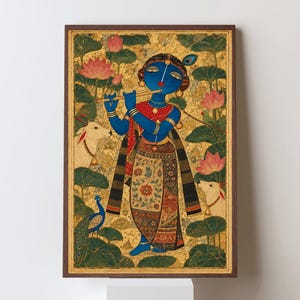 May include: A framed painting featuring a blue-skinned figure playing a flute, surrounded by pink lotus flowers, two white cows, and a peacock. The background is textured gold, and the figure wears a patterned skirt and jewellery in a vertical composition.