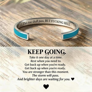 May include: A silver-coloured cuff bracelet featuring a bright turquoise inlay. The interior is engraved with the text: This too shall pass, BUT FUCKING HELL. Below the bracelet, text reads: KEEP GOING. Take it one day at a time. Rest when you need to.