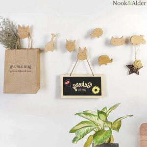 May include: Wooden animal-shaped wall hooks and a small chalkboard sign with the word "bakery" written on it. A brown paper bag hangs from a fox hook. The hooks include a giraffe, fox, lion, rabbit, elephant, and hippo.