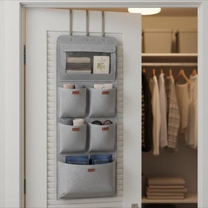 Könnte beinhalten: Ein grauer Tür-Organizer mit mehreren Taschen. Der Organizer hat einen transparenten oberen Bereich und mehrere Filztaschen in verschiedenen Größen. Einige Taschen enthalten gefaltete Gegenstände, andere Zubehör. Der Organizer hängt an einer weißen Tür.