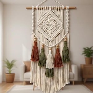 May include: Cream-colored macrame wall hanging with a geometric diamond pattern and wooden dowel. Features five tassels in shades of rust, olive green, and cream. A decorative piece for bohemian or modern home decor.